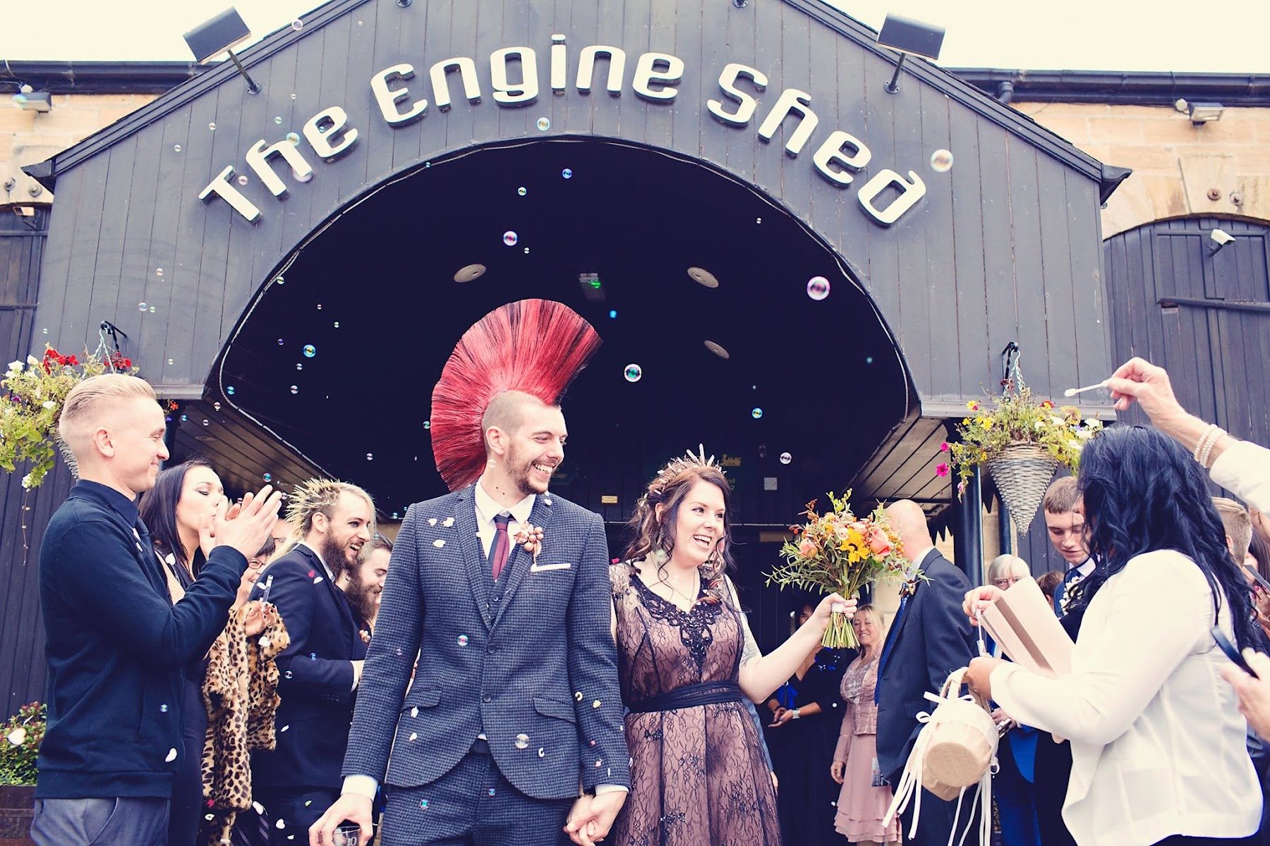 Guests throwing confetti over a couple outside the venue, under The Engine Shed sign