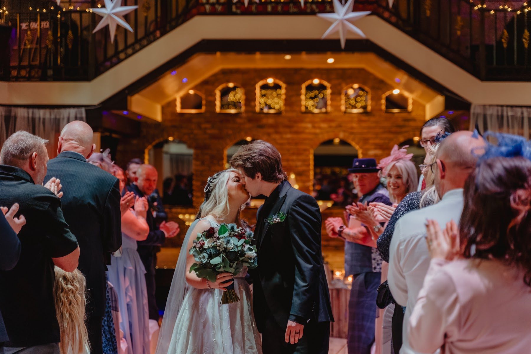 A couple kissing, ringed by their applauding guests