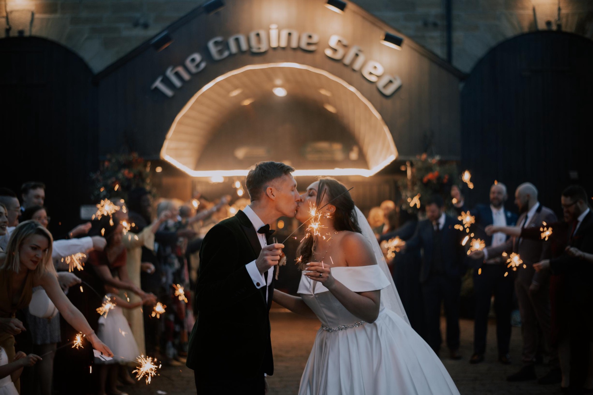 A couple share a sparkler kiss beneath the illuminated Engine Shed arch