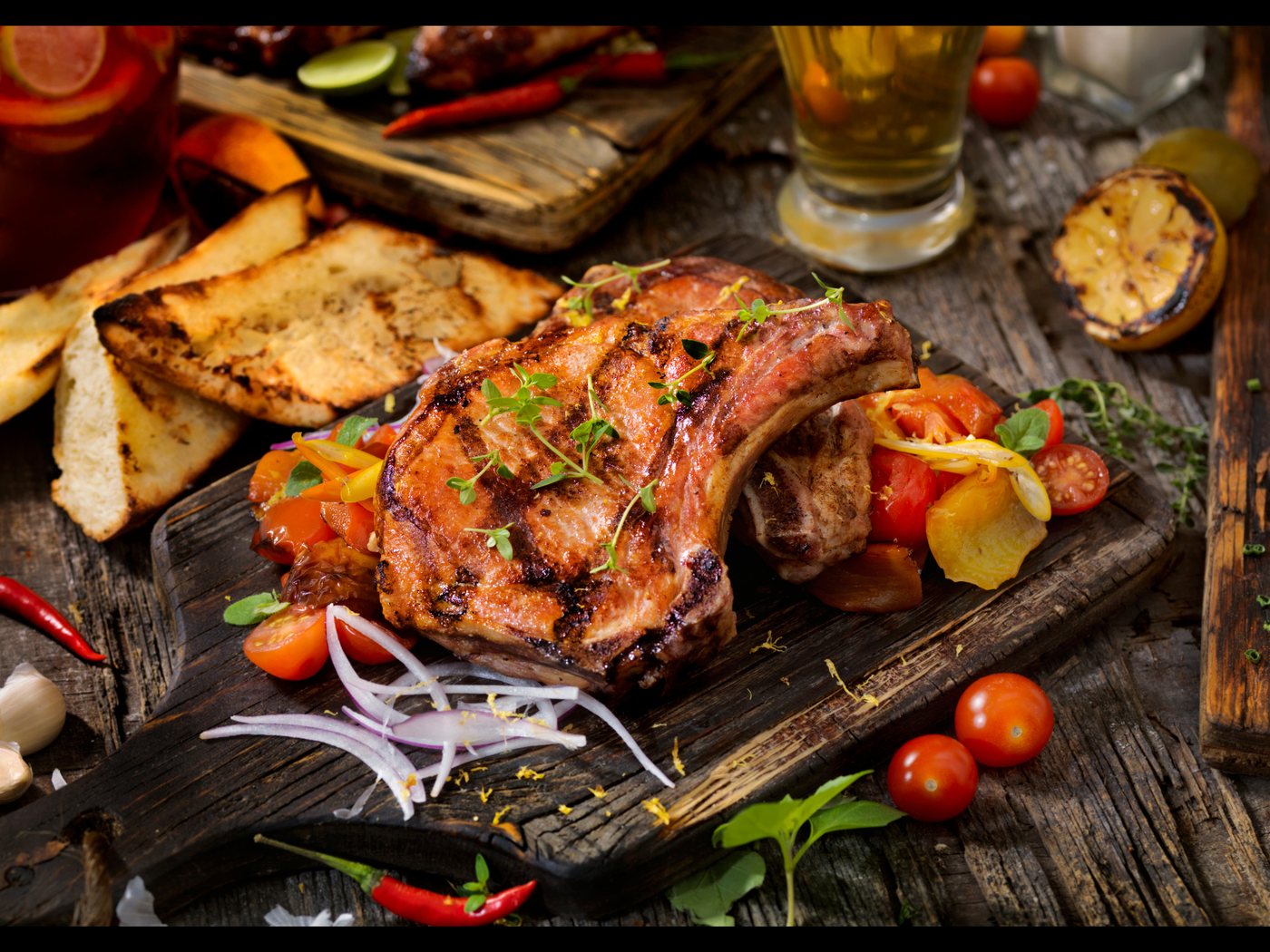 A barbecued chop with grilled peppers, tomatoes and flatbread on a wooden board