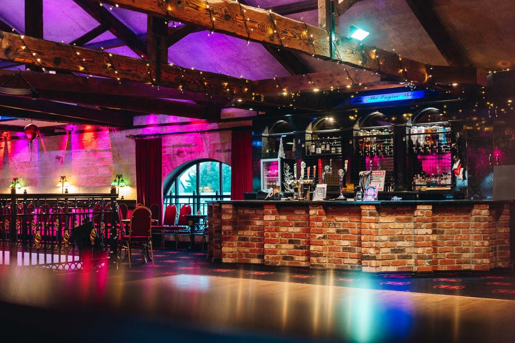 The bar and dance floor lit for an evening celebration beneath the beams