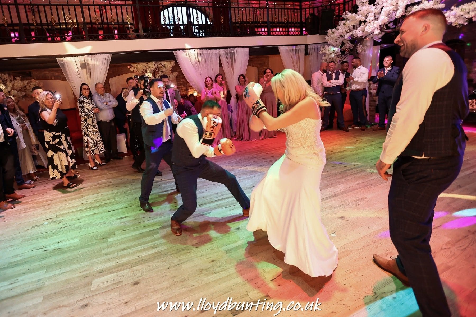 A newly married couple in boxing gloves squaring up on the dance floor as their guests watch