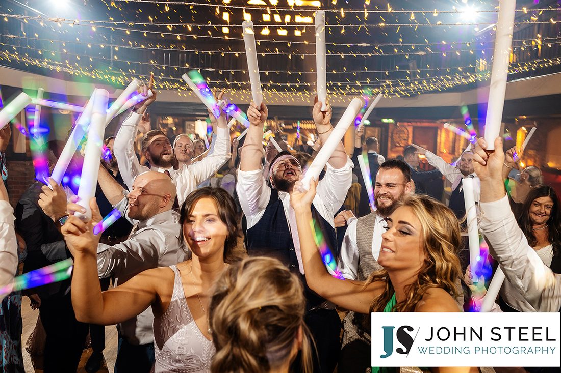 A packed crowd with glow sticks and hands in the air at a party