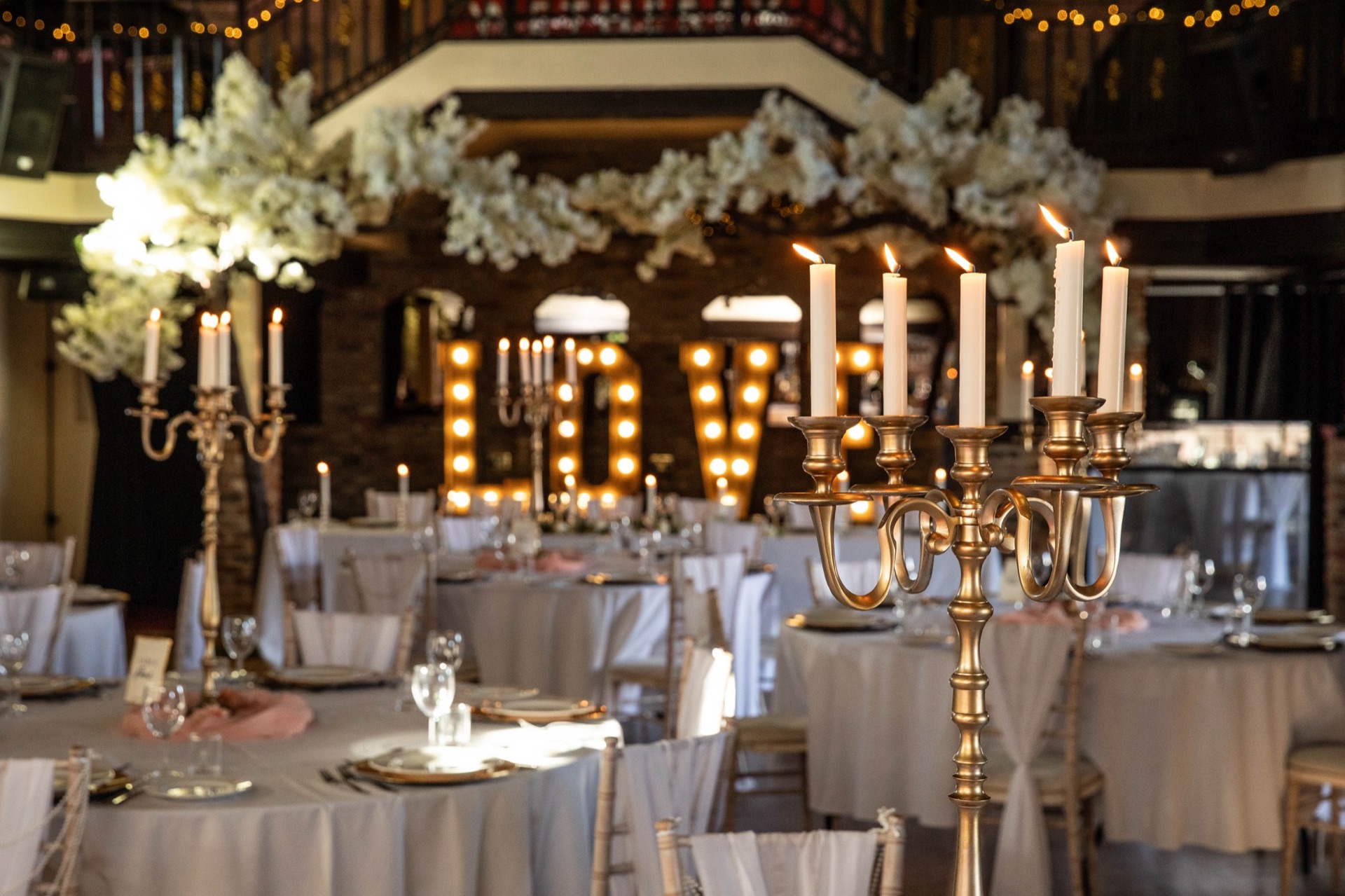 Illuminated LOVE letters and gold candelabra among the dressed tables
