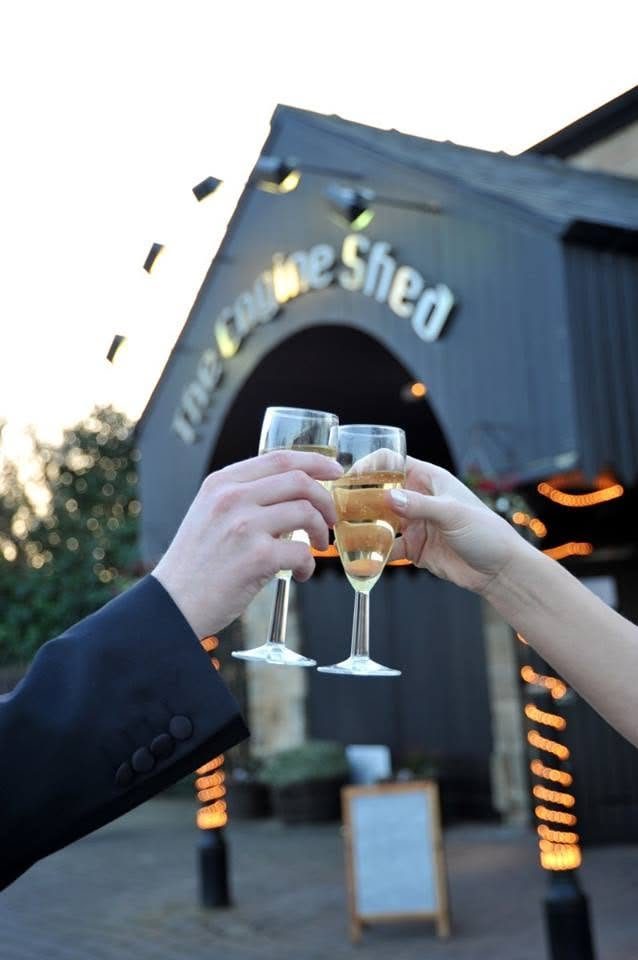 A couple raising a glass of champagne beneath the Engine Shed sign